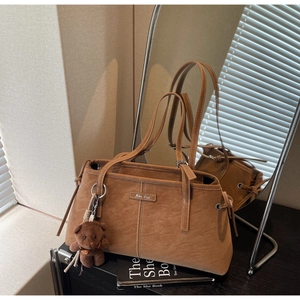 Detail view of brown leather tote bag with white stitching and cute teddy bear charm
