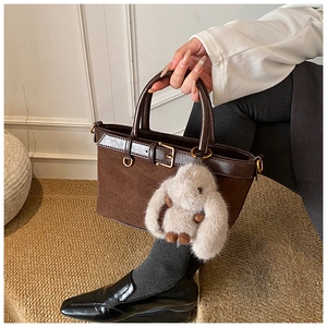 Brown suede bucket bag with leather handles and a grey plush rabbit charm detail