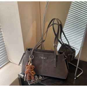 Detailed view of brown matte tote bag with contrast stitching and teddy bear charm