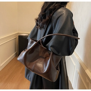 Detail of minimalist dark brown pleated tote bag with slim shoulder straps on a model
