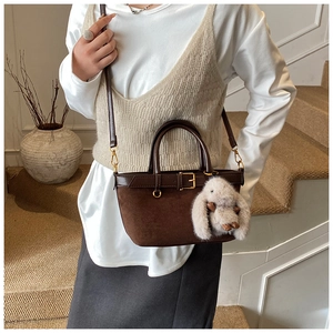 Brown leather handbag with plush rabbit charm and adjustable strap shown on stairs