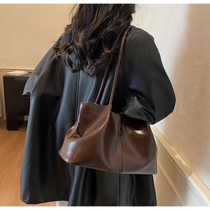 Detail of a large vintage brown tote bag with pleated texture worn on a female shoulder