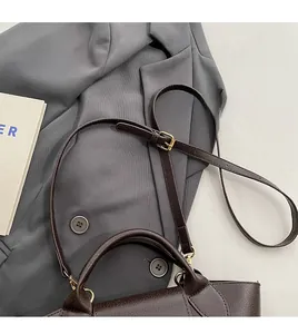 Detail of dark brown leather handbag featuring adjustable shoulder strap and gold hardware