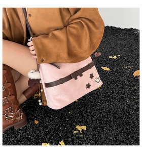 Pink faux suede shoulder bag with star embroidery and white pom-pom detail on dark stones