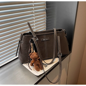 Detail of dark brown tote bag featuring white contrast stitching and plush bear charm