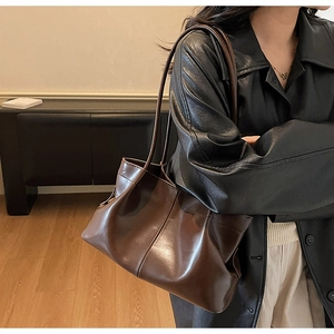 Side view of a dark brown large leather tote bag worn by a model in a minimalist room
