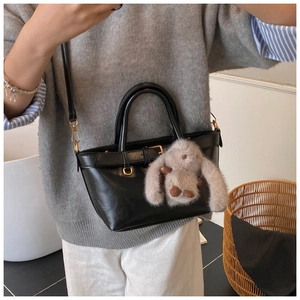 Detail of black leather bucket bag featuring gold hardware and a cute plush rabbit charm