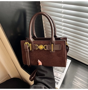 Detail of dark brown suede handbag with golden round buckle and sleek leather handle