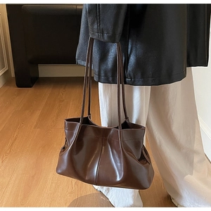 Detail of a brown pleated leather tote bag showing soft texture and slim shoulder strap