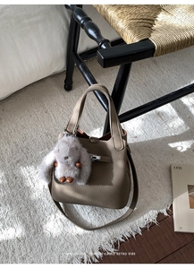 Detail of taupe lychee leather bucket bag with metal lock and plush rabbit pendant