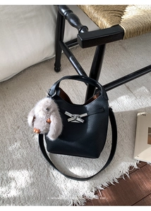 Detail of black lychee grain bucket bag featuring a cute plush bunny charm and silver buckle