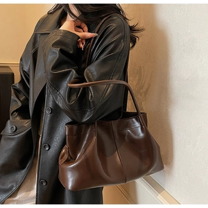 Close-up of deep coffee pleated tote bag worn on shoulder over a black leather coat