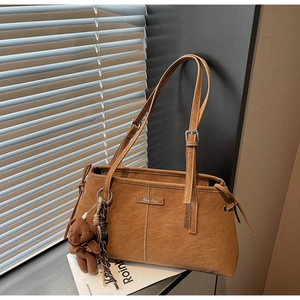 Detail of warm brown leather tote bag with sewing lines, plush bear charm and silk scarf