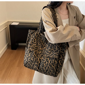 Detail of a large leopard print canvas tote bag with dual front pockets worn by a model