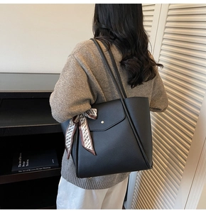 Detail of black pebbled leather tote bag with elegant vintage pattern silk scarf on handle