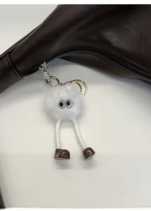 Close-up of white plush monster keychain with round eyes on a brown leather handbag