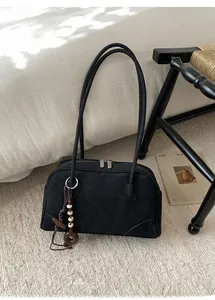 Detail of a minimalist black suede shoulder bag with retro beaded charm on a carpet