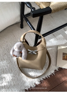 Detail of beige lychee pattern bucket bag with silver bow clasp and plush bunny charm