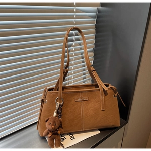 Detail of vintage brown tote bag with white stitching and plush bear charm decoration