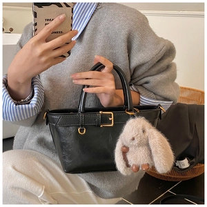 Detail of black leather tote bag featuring a golden buckle and grey plush rabbit charm