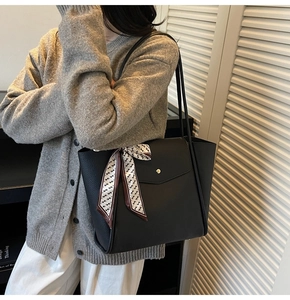 Close-up of a large black leather tote bag with silk scarf on handle and metal buckle detail