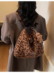 Large leopard print tote bag with brown straps and plush bear charm worn by a model