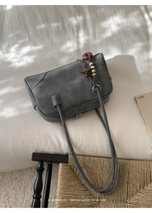 Detailed view of gray matte leather shoulder bag with vintage wooden bead charm accessory