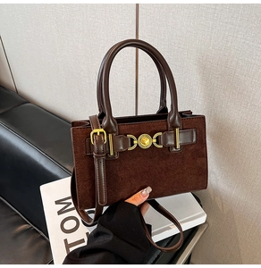 Close-up of brown suede handbag featuring a heart-shaped golden buckle and leather handles