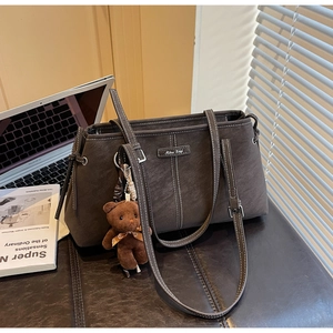 Detail of vintage gray-brown tote bag with white contrast stitching and plush bear charm