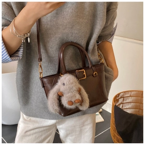 Detail of dark brown glossy leather tote with adjustable strap and plush rabbit charm