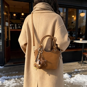Minimalist brown leather bucket bag with cute bear charm shown in a street style view