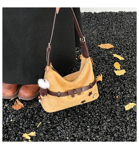 Detail of yellow suede tote bag with brown strap, star patches and white pompom charm
