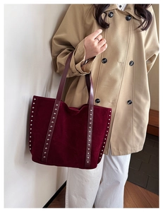 Large burgundy suede tote bag with silver studs worn by a model in a beige trench coat