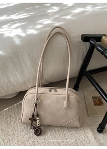 Detail view of beige suede Boston bag featuring long handles and beaded wood charm
