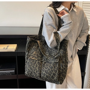 Detail of large canvas tote bag with green leopard print and front pockets on a model