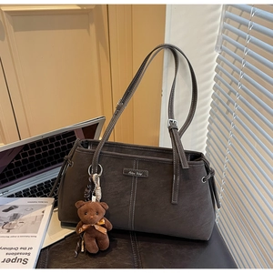 Detail of dark brown suede tote bag featuring white contrast stitching and a plush bear charm