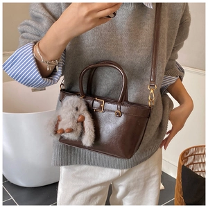 Detail of dark brown faux leather bucket bag with top handles and a plush rabbit charm