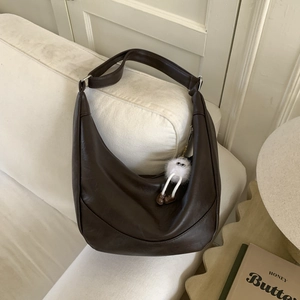 Dark brown crescent shoulder bag with cute white plush monster charm on a sofa armrest