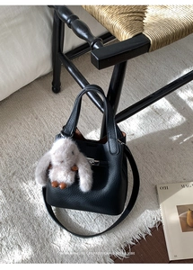 Detail of black lychee grain bucket bag with silver lock and plush bunny charm