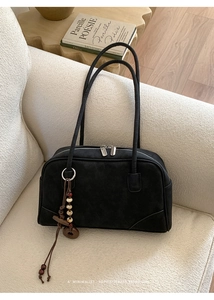 Close-up of black retro Boston bag with vintage wood charm on a textured white sofa