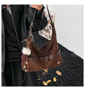 Detail of dark brown suede hobo bag with white fur ball charm and bow decoration