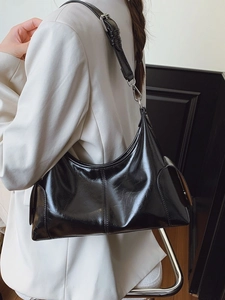 Minimalist black glossy leather crescent shoulder bag with adjustable strap worn by model