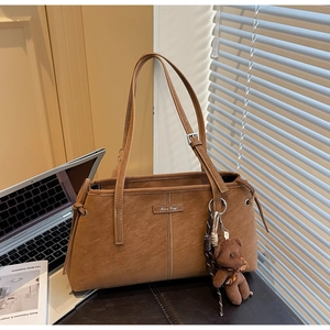 Close-up of vintage brown tote bag with stitching detail, metal logo and bear charm