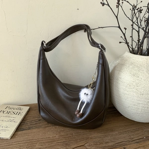 Detail of dark brown hobo bag with wide strap and cute plush monster charm on wood surface