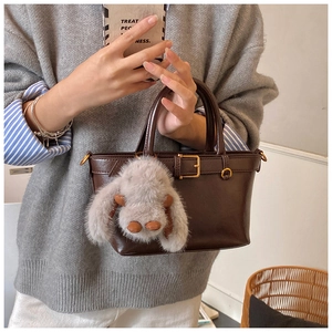 Detail view of brown matte leather handbag with gold buckle and cute bunny pendant