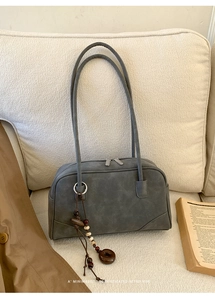 Close-up of a minimalist grey retro shoulder bag with a beaded tassel on a white sofa