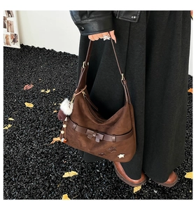 Detail of brown suede shoulder bag with star rivets, bow strap and plush bear charm