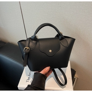 Detail of black lychee grain leather bucket bag with gold buckle and wave-shaped flap