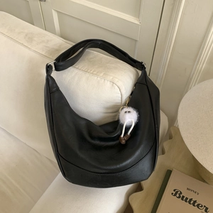 Detail of black leather hobo shoulder bag with a cute white plush monster charm