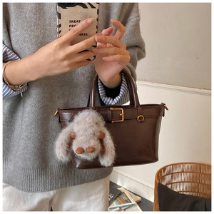 Detail of dark brown leather handbag featuring golden buckle and cute plush rabbit charm